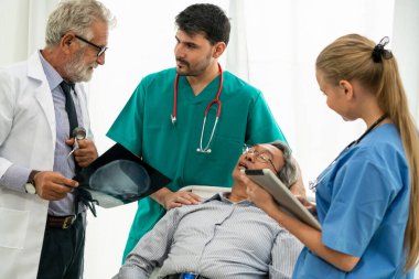 Doktor ekibi, hastane koğuş odasında yatakta yatan kıdemli yetişkin hastanın x ışını görüntüsü ile çalışır. Tıbbi grup ekip çalışması ve sağlık kişi personel hizmeti.