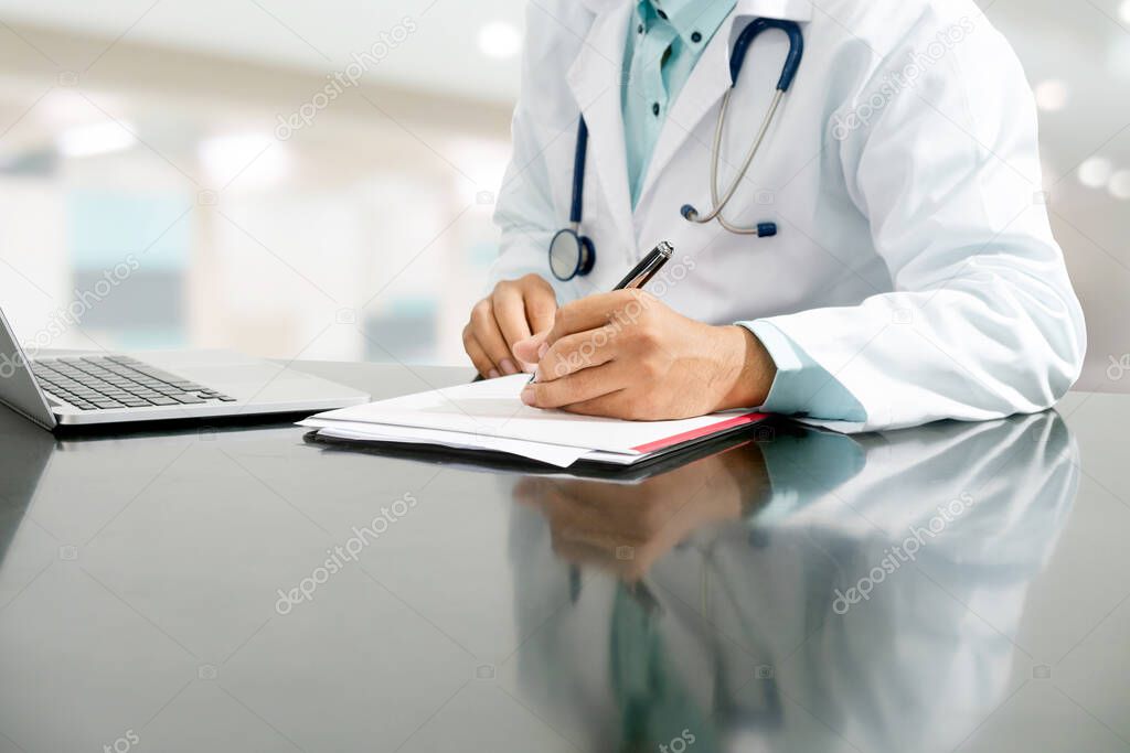 Doctor writes on documents at hospital office.