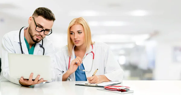 医者は病院で別の医師と議論しながらオフィスでラップトップ コンピューターでの作業します 医療と医師の医療サービス — ストック写真