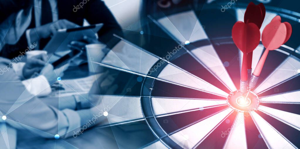 Business Target Goal For Success Strategy Concept - Red dart arrow hitting center goal on the dart board with business people working in background showing precision and success of business target.