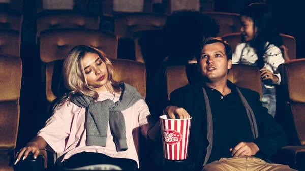 Audience walking to seats in the movie theater, watching film and eating popcorn.