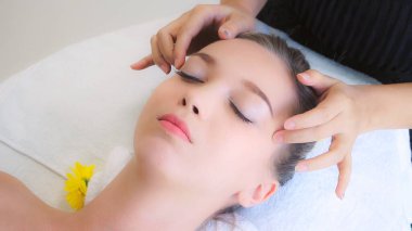 Lüks bir spa merkezinde masaj terapisti tarafından yüz masajı ve spa tedavisi için kaplıcaya uzanmış rahat bir kadın. Sağlık, stres atma ve gençleştirme kavramı.