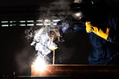 Fabrikada çelik kaynak makinesiyle çalışan metal kaynakçı güvenlik ekipmanı takıyor. El becerisi iş gücü kavramına göre metal imalatı ve inşaat bakım hizmeti.