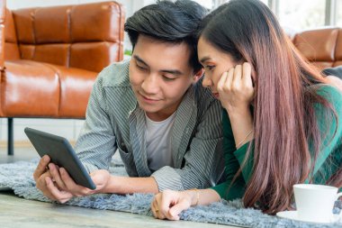 Mutlu Asyalı çift oturma odasında yerde yatarken tablet kullanıyor. Aşk ve ilişki kavramı.