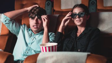 Sinemada üç boyutlu gözlüklü bir kadın ve erkek film izliyor. Ekrana bakar, heyecan verici ve patlamış mısır yer.