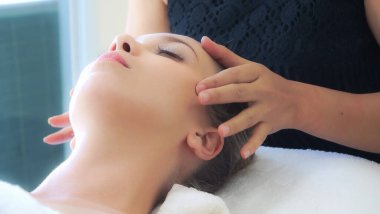 Lüks bir spa merkezinde masaj terapisti tarafından yüz masajı ve spa tedavisi için kaplıcaya uzanmış rahat bir kadın. Sağlık, stres atma ve gençleştirme kavramı.