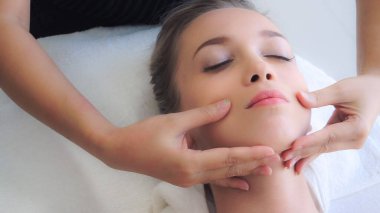 Lüks bir spa merkezinde masaj terapisti tarafından yüz masajı ve spa tedavisi için kaplıcaya uzanmış rahat bir kadın. Sağlık, stres atma ve gençleştirme kavramı.