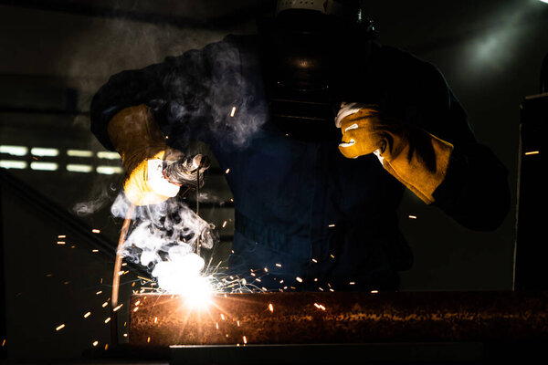 Metal welder working with arc welding machine to weld steel at factory while wearing safety equipment. Metalwork manufacturing and construction maintenance service by manual skill labor concept.