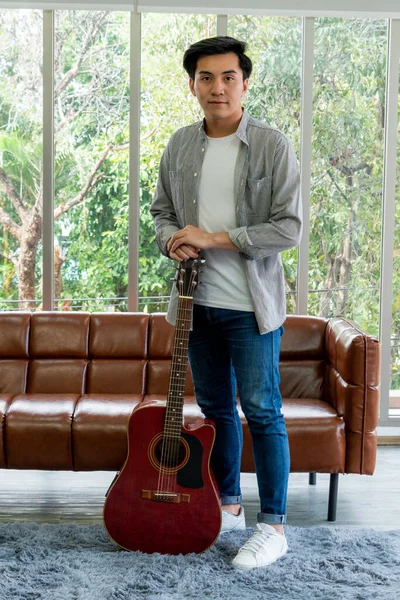 Young guitar player holding his guitar at home. Music and song concept.