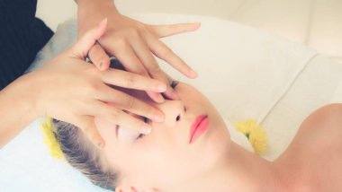 Lüks bir spa merkezinde masaj terapisti tarafından yüz masajı ve spa tedavisi için kaplıcaya uzanmış rahat bir kadın. Sağlık, stres atma ve gençleştirme kavramı.