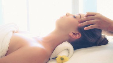 Lüks bir spa merkezinde masaj terapisti tarafından yüz masajı ve spa tedavisi için kaplıcaya uzanmış rahat bir kadın. Sağlık, stres atma ve gençleştirme kavramı.