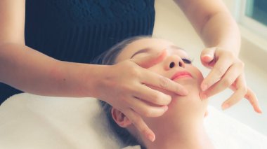 Lüks bir spa merkezinde masaj terapisti tarafından yüz masajı ve spa tedavisi için kaplıcaya uzanmış rahat bir kadın. Sağlık, stres atma ve gençleştirme kavramı.