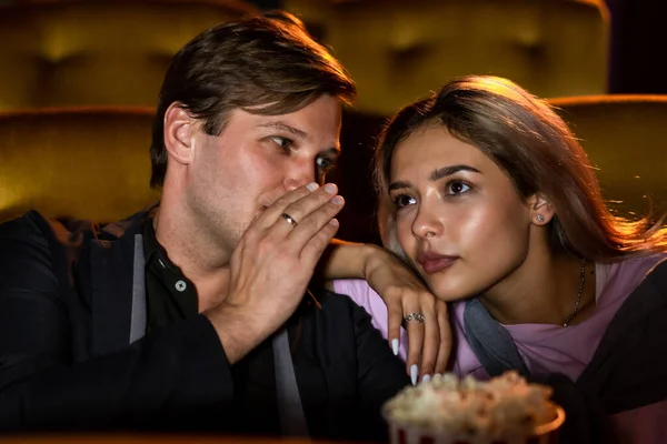 男は彼のガールフレンドにささやくと映画館で映画の中で話について何かを言う — ストック写真