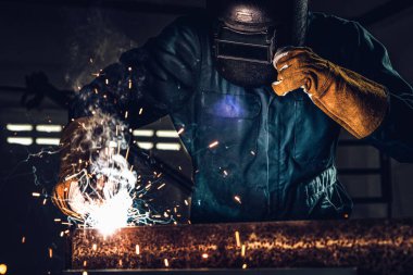 Fabrikada çelik kaynak makinesiyle çalışan metal kaynakçı güvenlik ekipmanı takıyor. El becerisi iş gücü kavramına göre metal imalatı ve inşaat bakım hizmeti.