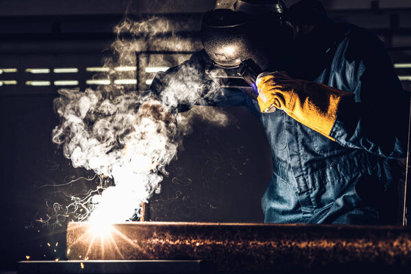 Metal welder working with arc welding machine to weld steel at factory while wearing safety equipment. Metalwork manufacturing and construction maintenance service by manual skill labor concept.