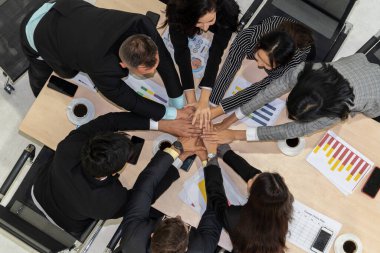 Mutlu iş adamları takım çalışmasının başarısını kutlarken ofis masasında yukarıdan çekilen neşeyle kutluyorlar. Genç işadamı ve işkadını işçiler birlik ve destek göstererek neşeli bir zafer kazandılar. .