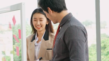 İş adamları ofisteki proje planlama kurulunda çalışıyor ve proje gelişimini analiz etmek için iş arkadaşlarıyla sohbet ediyorlar. Düzenli olması için cam duvara yapıştırılmış yapışkan notlar kullanıyorlar. .