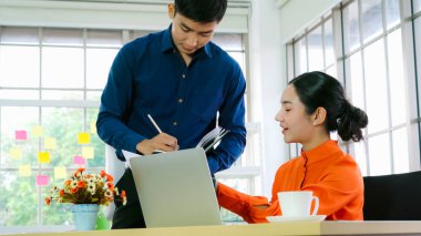 İki iş adamı toplantı odasında proje stratejisi hakkında konuşuyor. İş adamı, mali veri raporu hakkında sohbet ve tavsiyelerde bulunurken, modern işyerindeki iş arkadaşıyla proje planlamasını tartıştı.