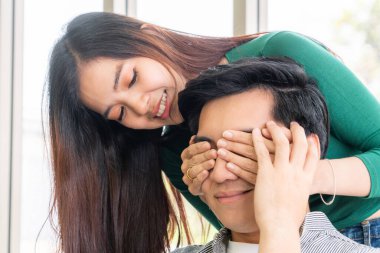 Mutlu Asyalı çift oturma odasında göz kapama oyunu oynuyor..