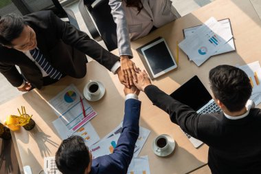 Mutlu iş adamları takım çalışmasının başarısını kutlarken ofis masasında yukarıdan çekilen neşeyle kutluyorlar. Genç işadamı ve işkadını işçiler birlik ve destek göstererek neşeli bir zafer kazandılar. .