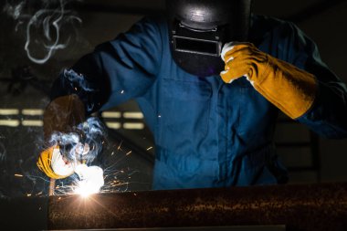 Fabrikada çelik kaynak makinesiyle çalışan metal kaynakçı güvenlik ekipmanı takıyor. El becerisi iş gücü kavramına göre metal imalatı ve inşaat bakım hizmeti.