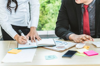 İki iş adamı toplantı odasında proje stratejisi hakkında konuşuyor. İş adamı, mali veri raporu hakkında sohbet ve tavsiyelerde bulunurken, modern işyerindeki iş arkadaşıyla proje planlamasını tartıştı.