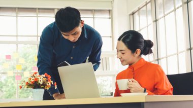 İki iş adamı toplantı odasında proje stratejisi hakkında konuşuyor. İş adamı, mali veri raporu hakkında sohbet ve tavsiyelerde bulunurken, modern işyerindeki iş arkadaşıyla proje planlamasını tartıştı.