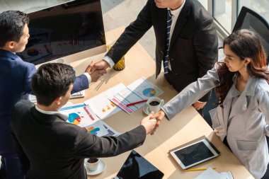 Grup iş adamları toplantı masasında el sıkışırken üst açıdan kendilerine güvenirler. Genç işadamı ve işkadını işçiler yatırım anlaşması imzaladılar.