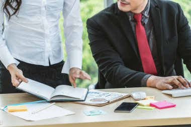 İki iş adamı toplantı odasında proje stratejisi hakkında konuşuyor. İş adamı, mali veri raporu hakkında sohbet ve tavsiyelerde bulunurken, modern işyerindeki iş arkadaşıyla proje planlamasını tartıştı.