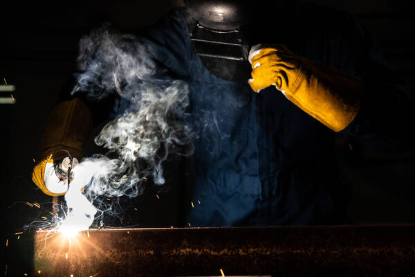 Metal welder working with arc welding machine to weld steel at factory while wearing safety equipment. Metalwork manufacturing and construction maintenance service by manual skill labor concept.