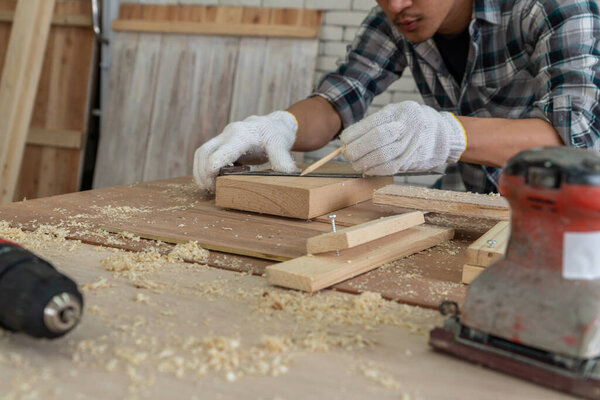 Carpenter working on wood craft at workshop to produce construction material or wooden furniture. The young Asian carpenter use professional tools for crafting. DIY maker and carpentry work concept.