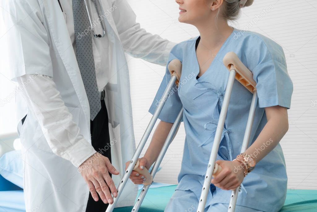 Doctor takes care of patient in crutch at hospital. Physical therapist and leg injury recovery concept.