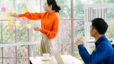 İş adamları ofisteki proje planlama kurulunda çalışıyor ve proje gelişimini analiz etmek için iş arkadaşlarıyla sohbet ediyorlar. Düzenli olması için cam duvara yapıştırılmış yapışkan notlar kullanıyorlar. .