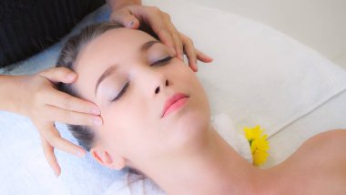 Lüks bir spa merkezinde masaj terapisti tarafından yüz masajı ve spa tedavisi için kaplıcaya uzanmış rahat bir kadın. Sağlık, stres atma ve gençleştirme kavramı.