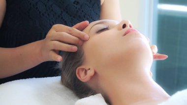 Lüks bir spa merkezinde masaj terapisti tarafından yüz masajı ve spa tedavisi için kaplıcaya uzanmış rahat bir kadın. Sağlık, stres atma ve gençleştirme kavramı.