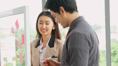 İş adamları ofisteki proje planlama kurulunda çalışıyor ve proje gelişimini analiz etmek için iş arkadaşlarıyla sohbet ediyorlar. Düzenli olması için cam duvara yapıştırılmış yapışkan notlar kullanıyorlar. .