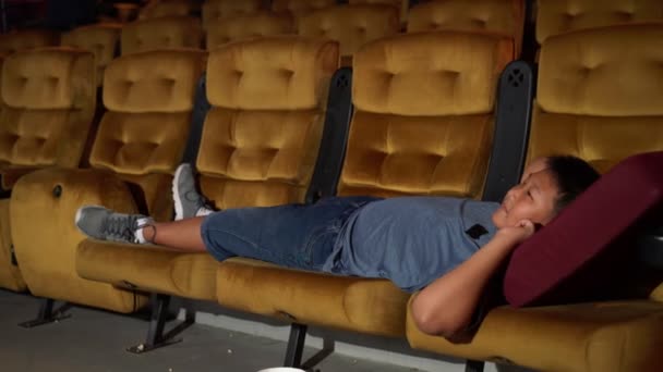 Мальчик лежит на кресле в кино. — стоковое видео