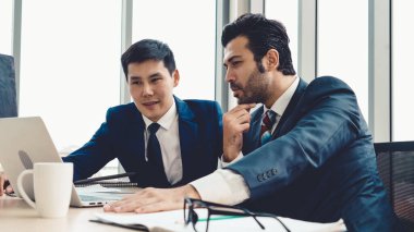 İki iş adamı toplantı odasında proje stratejisi hakkında konuşuyor. İş adamı, mali veri raporu hakkında sohbet ve tavsiyelerde bulunurken, modern işyerindeki iş arkadaşıyla proje planlamasını tartıştı.