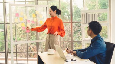 İş adamları ofisteki proje planlama kurulunda çalışıyor ve proje gelişimini analiz etmek için iş arkadaşlarıyla sohbet ediyorlar. Düzenli olması için cam duvara yapıştırılmış yapışkan notlar kullanıyorlar. .