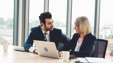 İki iş adamı toplantı odasında proje stratejisi hakkında konuşuyor. İş adamı, mali veri raporu hakkında sohbet ve tavsiyelerde bulunurken, modern işyerindeki iş arkadaşıyla proje planlamasını tartıştı.