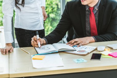 İki iş adamı toplantı odasında proje stratejisi hakkında konuşuyor. İş adamı, mali veri raporu hakkında sohbet ve tavsiyelerde bulunurken, modern işyerindeki iş arkadaşıyla proje planlamasını tartıştı.