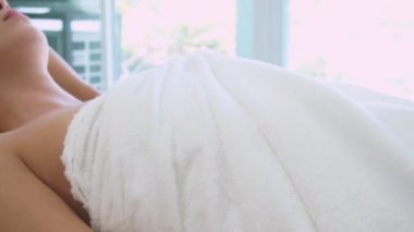 Rahatlamış genç bir kadın masaj için spa yatağında yatıyor..