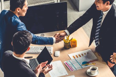 Grup iş adamları toplantı masasında el sıkışırken üst açıdan kendilerine güvenirler. Genç işadamı ve işkadını işçiler yatırım anlaşması imzaladılar.