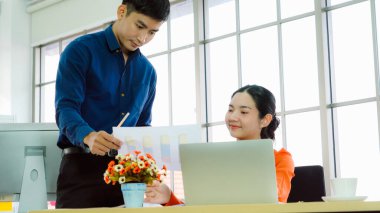 İki iş adamı toplantı odasında proje stratejisi hakkında konuşuyor. İş adamı, mali veri raporu hakkında sohbet ve tavsiyelerde bulunurken, modern işyerindeki iş arkadaşıyla proje planlamasını tartıştı.