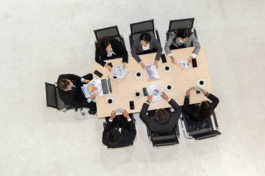 İş adamları grup toplantısı ofiste yukarıdan çekildi. İş kadınları, iş adamları ve ofis çalışanları, proje planlama belgeleriyle takım konferansında toplantı masasında çalışıyorlar. .