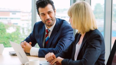 İki iş adamı toplantı odasında proje stratejisi hakkında konuşuyor. İş adamı, mali veri raporu hakkında sohbet ve tavsiyelerde bulunurken, modern işyerindeki iş arkadaşıyla proje planlamasını tartıştı.