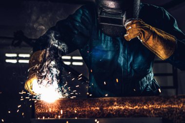 Fabrikada çelik kaynak makinesiyle çalışan metal kaynakçı güvenlik ekipmanı takıyor. El becerisi iş gücü kavramına göre metal imalatı ve inşaat bakım hizmeti.