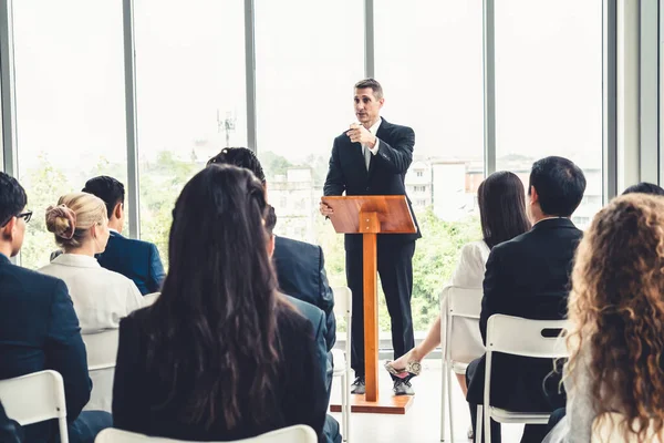 Group of business people meeting in a seminar conference . Audience listening to instructor in employee education training session . Office worker community summit forum with expert speaker .