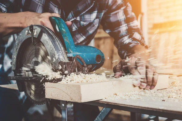 Carpenter working on wood craft at workshop to produce construction material or wooden furniture. The young Asian carpenter use professional tools for crafting. DIY maker and carpentry work concept.