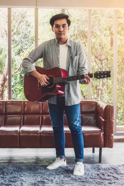 Young guitar player holding his guitar at home. Music and song concept.